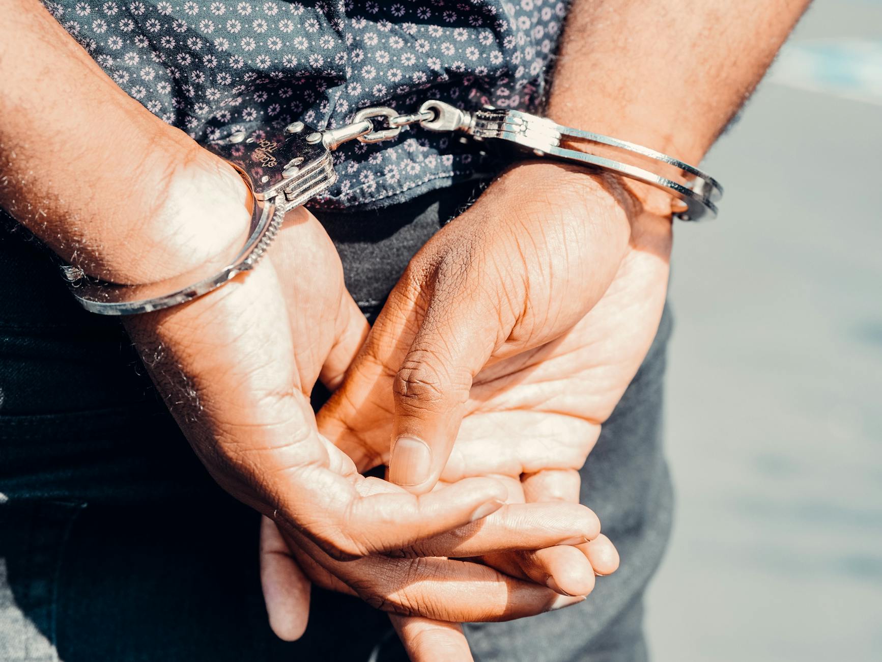 Close-up of an adult male's hands in handcuffs, symbolizing law enforcement and justice.
